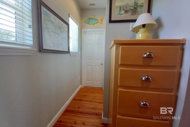 hallway with light wood-style floors, visible vents, and baseboards