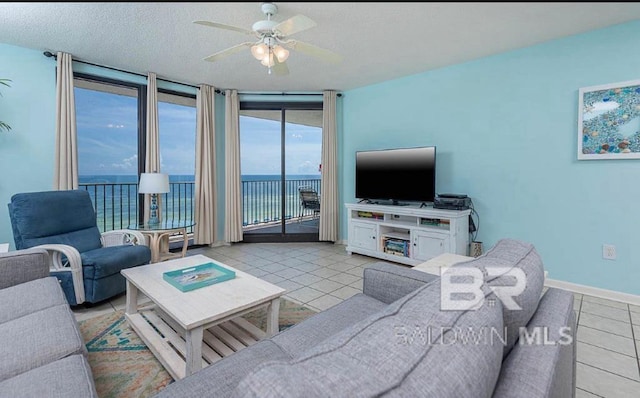 living room featuring ceiling fan, light tile patterned flooring, a textured ceiling, floor to ceiling windows, and a water view