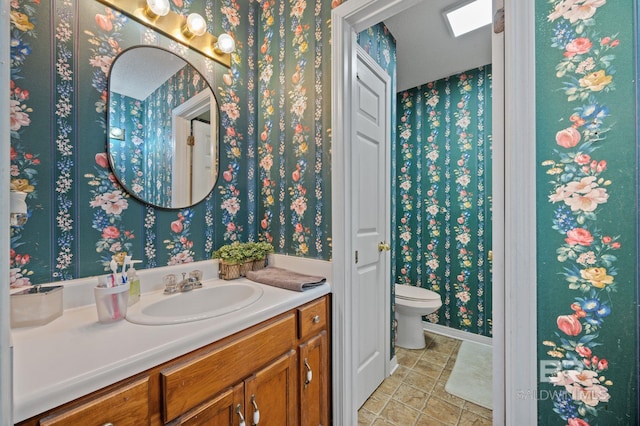 bathroom with a skylight, vanity, toilet, and wallpapered walls