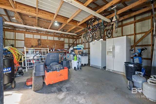 garage featuring white fridge with ice dispenser, metal wall, and freestanding refrigerator