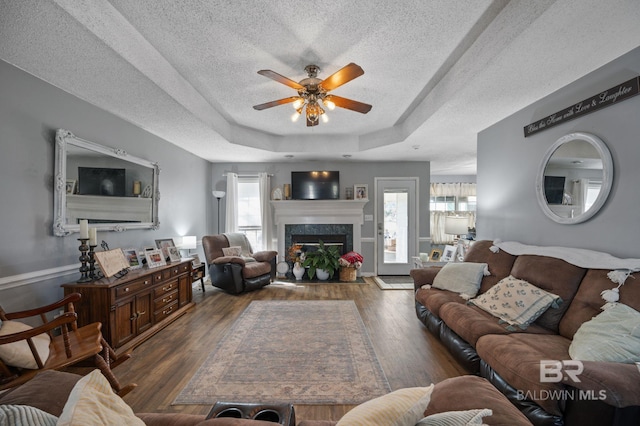 living room with a textured ceiling, a tray ceiling, a fireplace with raised hearth, and wood finished floors