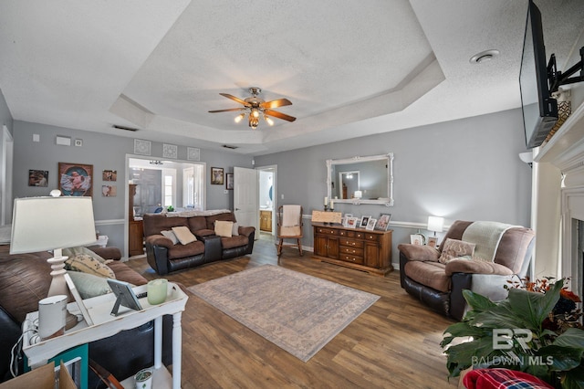 living area featuring a textured ceiling, wood finished floors, a raised ceiling, and visible vents