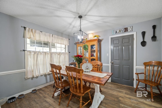 dining space with a textured ceiling, a notable chandelier, wood finished floors, and baseboards