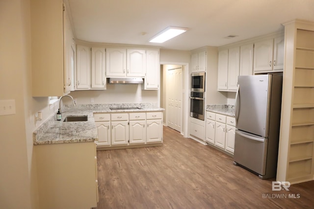 kitchen with under cabinet range hood, appliances with stainless steel finishes, a sink, and light wood-style flooring