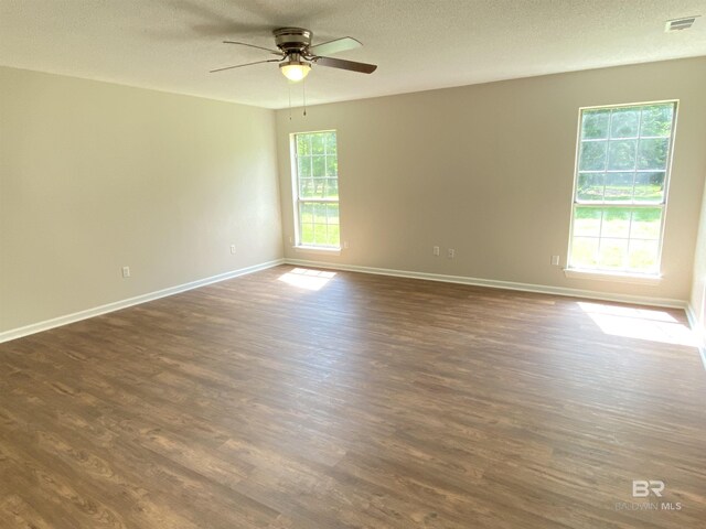 empty room featuring visible vents, dark wood-style flooring, baseboards, ceiling fan, and a textured ceiling