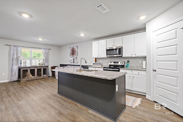 kitchen with white cabinets, appliances with stainless steel finishes, light wood-type flooring, and an island with sink