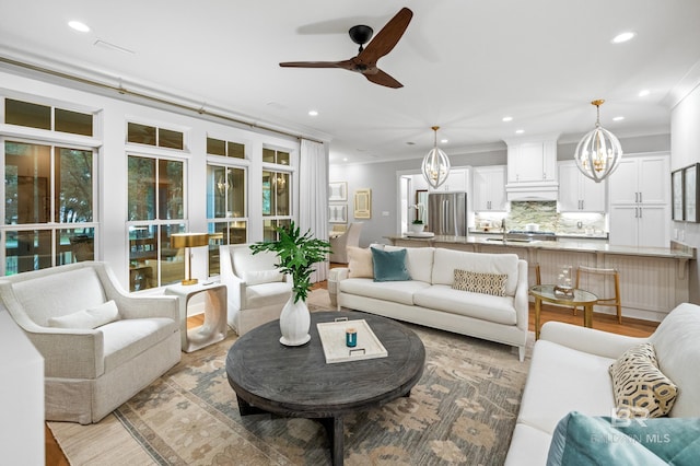 living room with ceiling fan with notable chandelier, light hardwood / wood-style floors, and ornamental molding