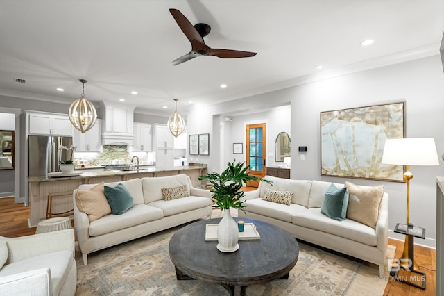 living room featuring ceiling fan, sink, light wood-type flooring, and crown molding