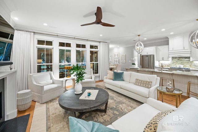 living room with sink, light hardwood / wood-style floors, ceiling fan with notable chandelier, and ornamental molding