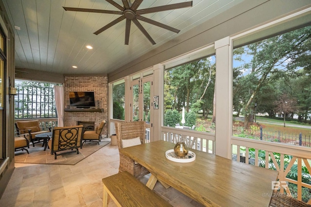 sunroom / solarium with a fireplace, ceiling fan, a healthy amount of sunlight, and wood ceiling