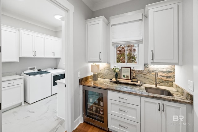 kitchen with sink, beverage cooler, washing machine and dryer, dark stone countertops, and white cabinets