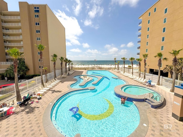 view of pool with fence, a pool with connected hot tub, a beach view, a water view, and a patio area