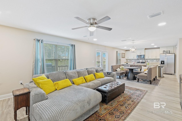 living room featuring ceiling fan with notable chandelier and light hardwood / wood-style flooring