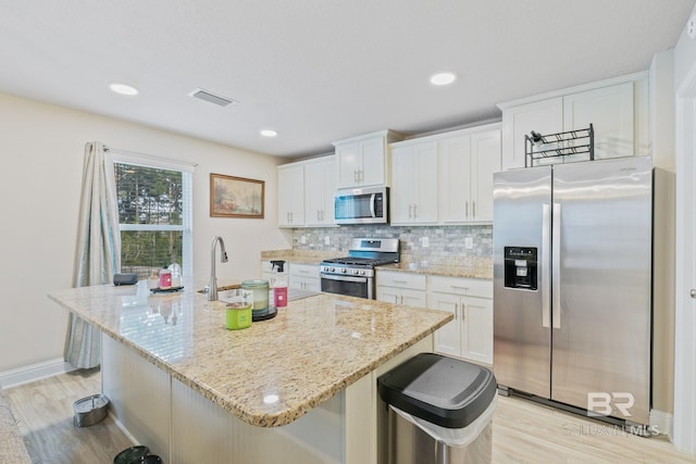 kitchen with appliances with stainless steel finishes, light wood-type flooring, a kitchen island with sink, and white cabinets