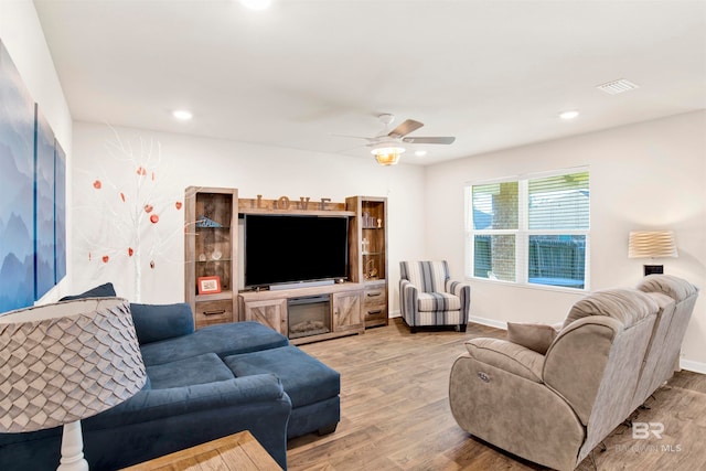 living room featuring ceiling fan, a fireplace, and light wood-type flooring