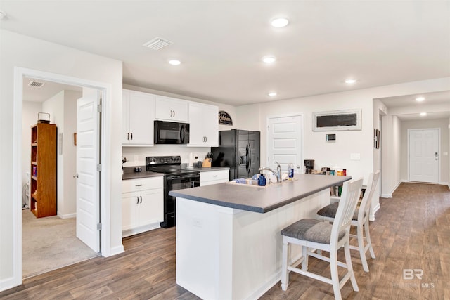 kitchen featuring white cabinetry, dark hardwood / wood-style flooring, a kitchen bar, a kitchen island with sink, and black appliances