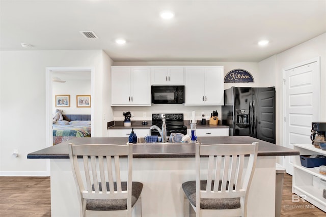 kitchen with white cabinetry, dark wood-type flooring, a kitchen breakfast bar, a center island with sink, and black appliances