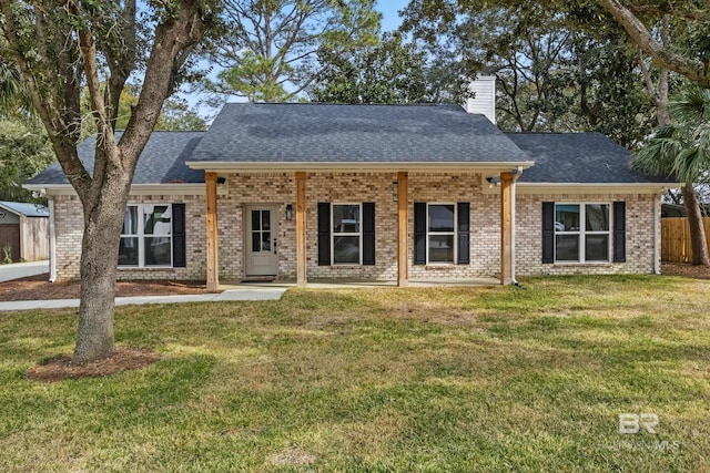 view of front of property featuring a front yard, brick siding, a chimney, and roof with shingles