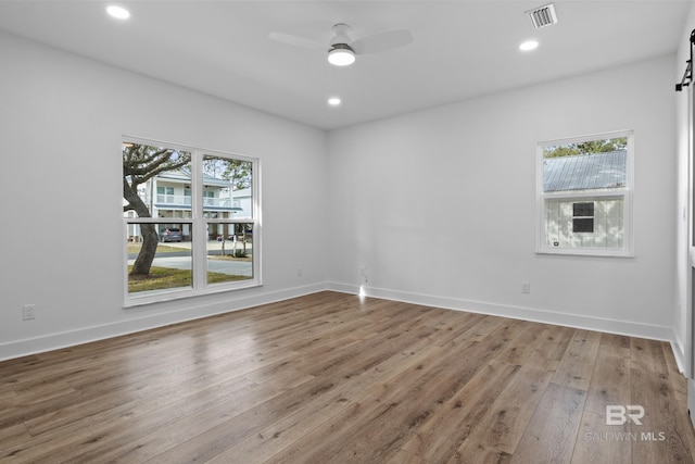 empty room featuring ceiling fan, visible vents, a wealth of natural light, and wood finished floors