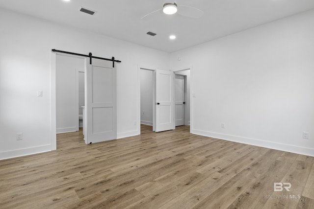 unfurnished bedroom featuring light wood-type flooring, a barn door, visible vents, and baseboards