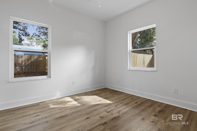 spare room with a ceiling fan, a wealth of natural light, baseboards, and wood finished floors