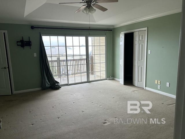 empty room with a tray ceiling, carpet, crown molding, ceiling fan, and baseboards