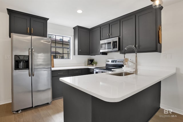 kitchen with light wood-type flooring, recessed lighting, stainless steel appliances, a peninsula, and light countertops