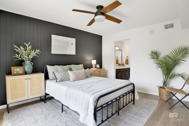 bedroom featuring visible vents, ceiling fan, baseboards, ensuite bathroom, and wood finished floors