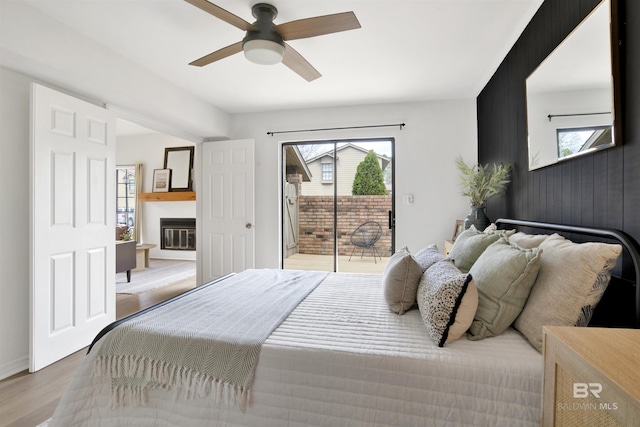 bedroom featuring baseboards, wood finished floors, a glass covered fireplace, a ceiling fan, and access to outside