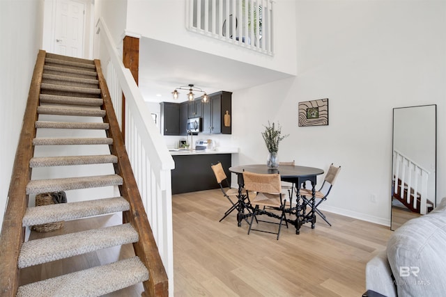 dining area with baseboards, a high ceiling, light wood-style flooring, and stairs