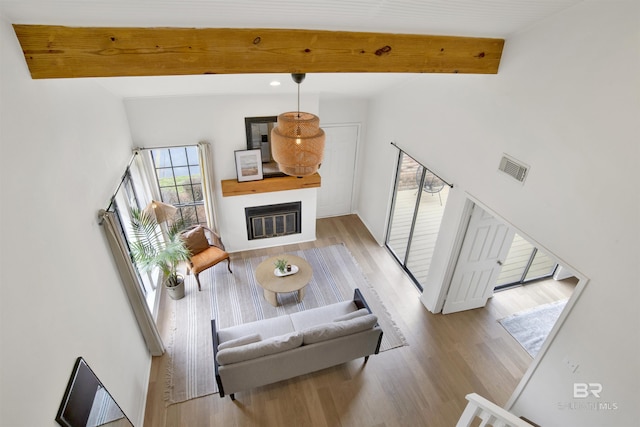 living room featuring visible vents, beamed ceiling, wood finished floors, a glass covered fireplace, and high vaulted ceiling