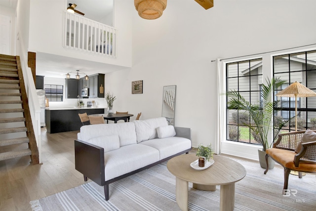 living room featuring stairway, light wood-style floors, a towering ceiling, and ceiling fan