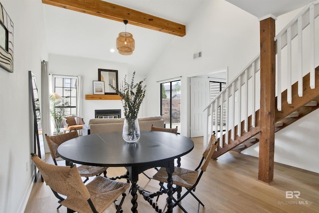 dining room featuring visible vents, beam ceiling, a wealth of natural light, a glass covered fireplace, and high vaulted ceiling