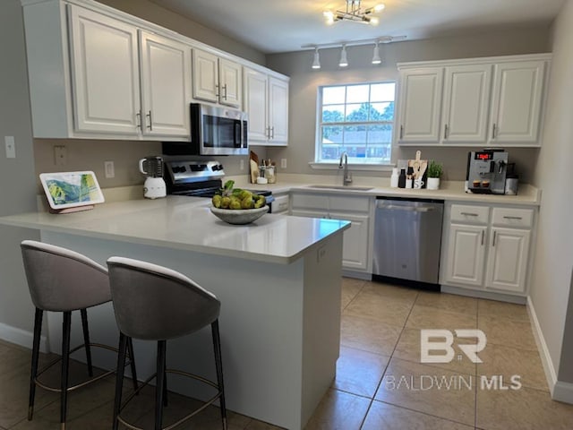 16825 Edward Dr, Gulf Shores, AL 36542 - kitchen featuring appliances with stainless steel finishes, a sink, a kitchen bar, a peninsula, and white cabinets