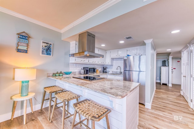 kitchen with a breakfast bar area, island range hood, kitchen peninsula, stainless steel appliances, and white cabinets