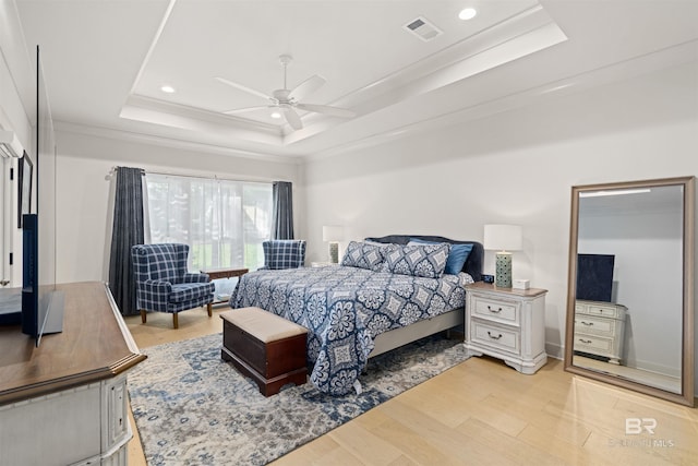 bedroom with light hardwood / wood-style floors, a raised ceiling, ceiling fan, and ornamental molding