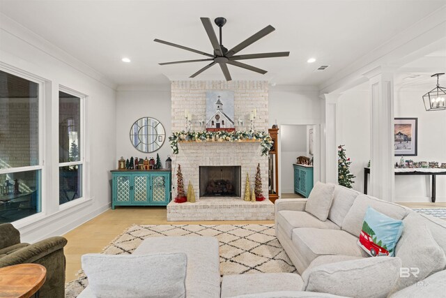 living room with a brick fireplace, ceiling fan with notable chandelier, ornamental molding, and light hardwood / wood-style flooring