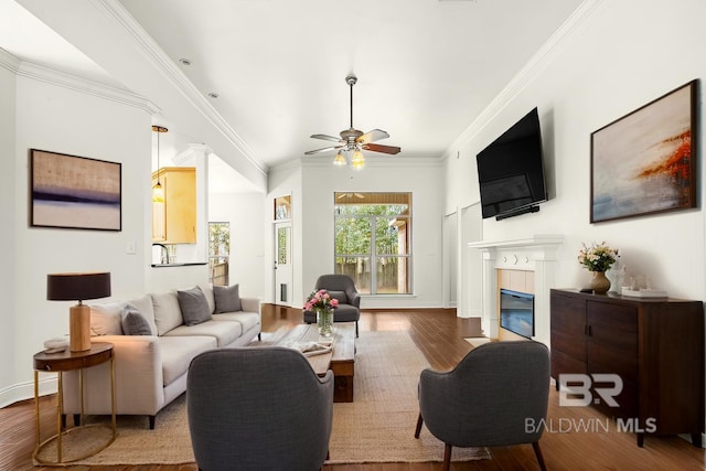 living room with baseboards, ornamental molding, wood finished floors, and a glass covered fireplace