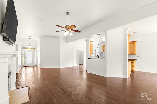 unfurnished living room featuring baseboards, ceiling fan, ornamental molding, wood finished floors, and ornate columns