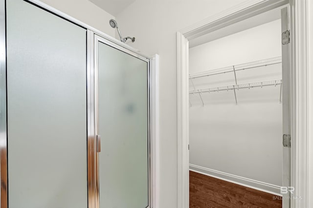 full bath featuring a stall shower, a spacious closet, baseboards, and wood finished floors