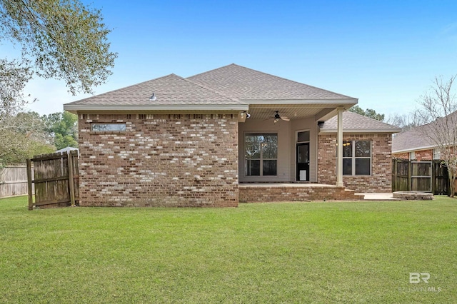 back of house featuring brick siding, ceiling fan, a lawn, and fence