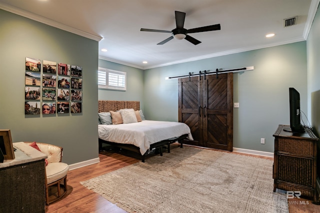 bedroom with ornamental molding, a barn door, ceiling fan, and light hardwood / wood-style flooring