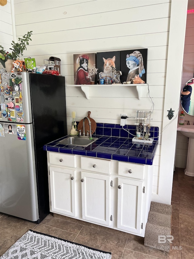 kitchen with tile countertops, stainless steel refrigerator, sink, white cabinets, and dark tile patterned flooring