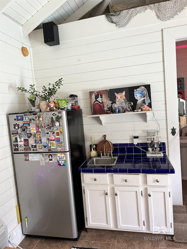 kitchen with lofted ceiling, sink, tile counters, stainless steel fridge, and white cabinets