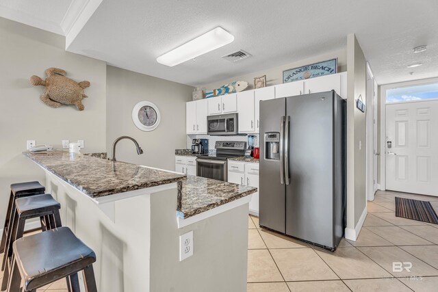 27284 Gulf Rd Unit 711, Orange Beach, AL 36561 - kitchen featuring appliances with stainless steel finishes, a breakfast bar, a peninsula, white cabinetry, and light tile patterned floors