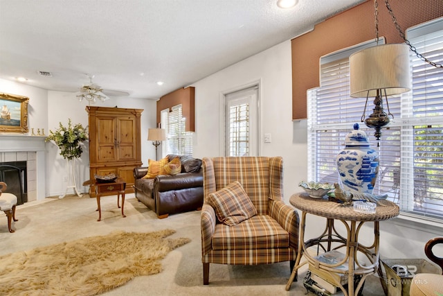 sitting room featuring a tiled fireplace, ceiling fan, carpet, and a textured ceiling