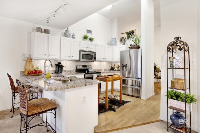 kitchen featuring stainless steel appliances, light stone counters, kitchen peninsula, a breakfast bar, and white cabinets