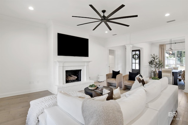 living room featuring ornate columns, a fireplace, ceiling fan, light hardwood / wood-style floors, and crown molding