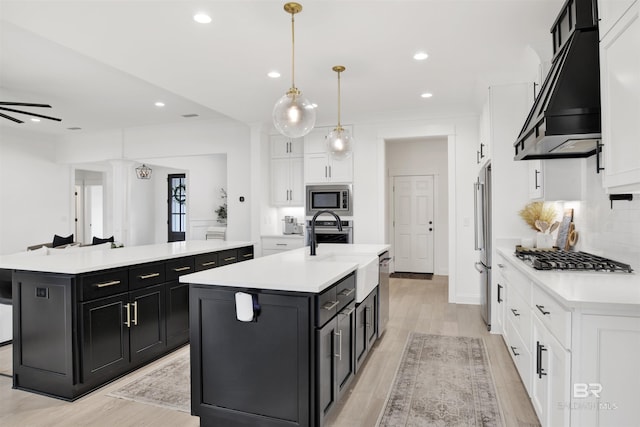 kitchen featuring premium range hood, decorative light fixtures, white cabinetry, a kitchen island with sink, and stainless steel appliances