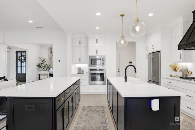 kitchen featuring sink, hanging light fixtures, custom range hood, stainless steel appliances, and a kitchen island with sink